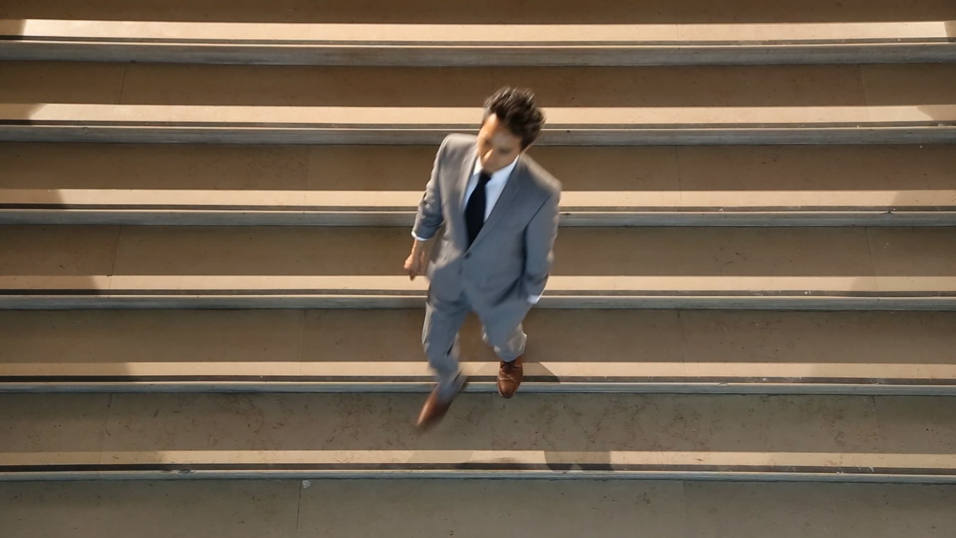 Still from the film Network/Intersect, by Ollie Palmer. The image depicts a businessman in a suit descending a flight of stairs.